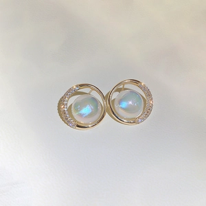 Detailed macro view of gold-plated circular earrings with zircons and aurora faux pearls