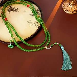 Détail d'un collier de perles style chinois avec perles vertes et long pompon en soie