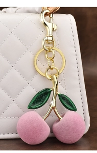 Close-up of pink plush cherry keychain with gold stem on a white quilted handbag