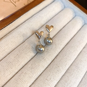 Détail de boucles d'oreilles cœur en perle grise sur un plateau à bijoux en tissu
