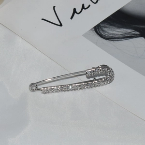 Sparkling silver safety pin brooch with clear rhinestones on white silk fabric
