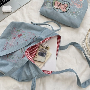 Detail of denim tote bag with star embroidery, red gingham lining and drawstring closure