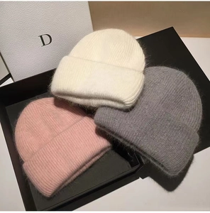 Detailed texture of white, pink, and grey rabbit fur knit beanies on a gift box