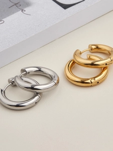 Polished gold and silver stainless steel hoop earrings on light leather background