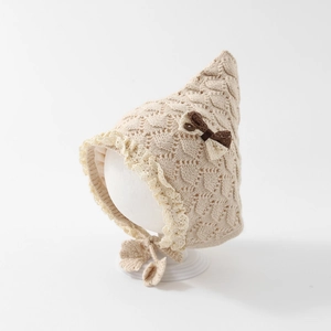 Detail of beige knit baby bonnet with delicate lace trim and ribbon bow decoration