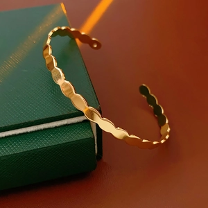 Detail of a wavy-edged gold cuff bracelet placed on a dark green leather jewelry box