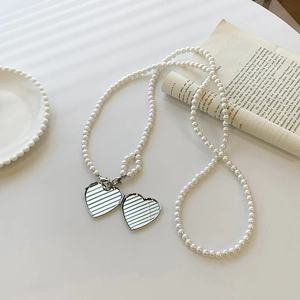 Elegant pearl necklace with silver heart pendants on white surface with artistic shadows