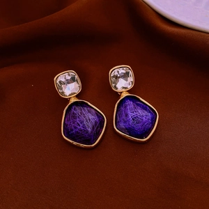 Detail view of purple resin earrings with golden metal edges and silk texture