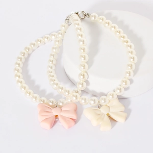 Close-up of pink and cream pearl pet collars with resin bow pendants on a white display