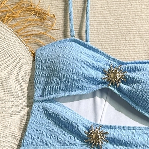 Detail of light blue textured swimwear featuring golden sun metal buckles and thin straps