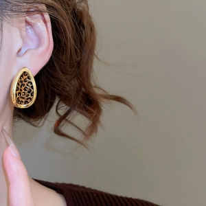 Close-up of gold-rimmed leopard print leaf earrings worn by a model in a minimal setting