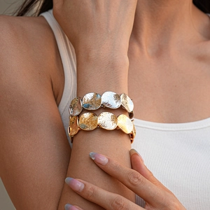 Dettaglio di braccialetti a dischi martellati oro e argento sul polso di una modella