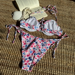 Flachbild von Bikini-Set mit kleinem Blumendruck, Bügel-Top und seitlich gebundener Hose auf Matte