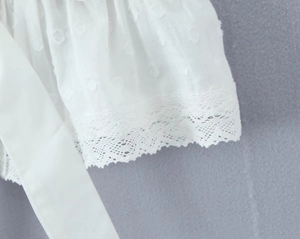 Détail du tissu blanc avec pois texturés, dentelle délicate et ruban à nouer
