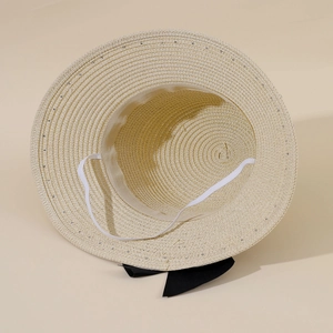 Detail view of beige straw hat with sequins, bow tie, and white elastic chin strap