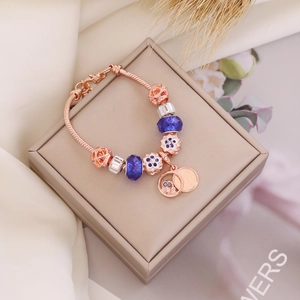 Rose gold owl charm bracelet with blue glass beads on display box with floral accents