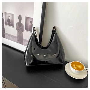 Close-up of black glossy patent leather baguette bag with golden buckle in cafe setting