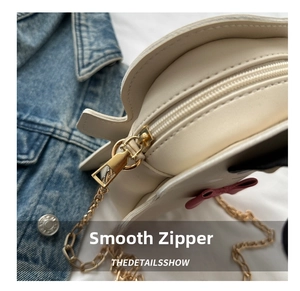 Detail showing smooth gold-tone zipper and pink bow on creamy white chain bag