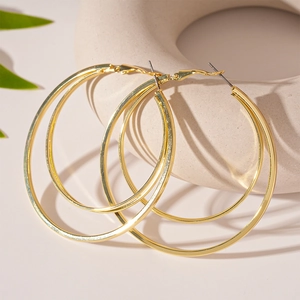 Macro detail of gold-plated double hoop earrings on a minimalist stone display with leaves