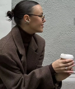 Close-up of metallic layered ear cuffs and diamond rings styled with a brown coat