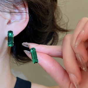 Close-up of elegant rectangular emerald green zirconia stud earrings worn on ear