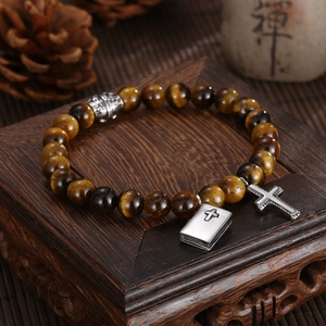 Detailaufnahme von Tigerauge-Armband mit Silberkreuz und Bibel-Anhängern auf Holz