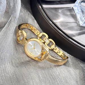 Detail of vintage gold bracelet watch with oval dial resting on grey textured fabric