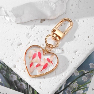 Heart-shaped resin keychain with dried pink flowers and gold metal frame on white stone