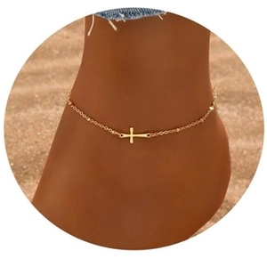 Close-up of golden cross charm anklet worn on ankle against a sunny beach background