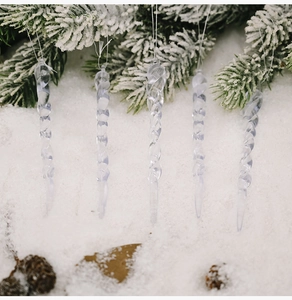 Detailed view of clear acrylic icicle ornaments hanging from a snowy Christmas branch