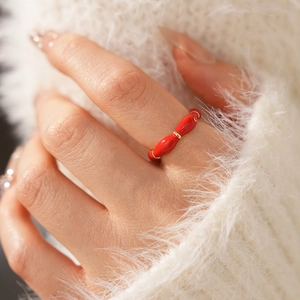 Detail of red enamel oval ring with gold plated accents worn on a hand over a sweater