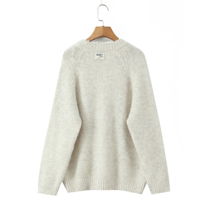 Close-up of cream knit sweater showing thick texture and round neck with designer label