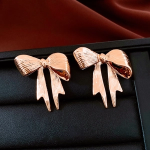 Detail of rose gold bow earrings with metal texture on black box and red velvet