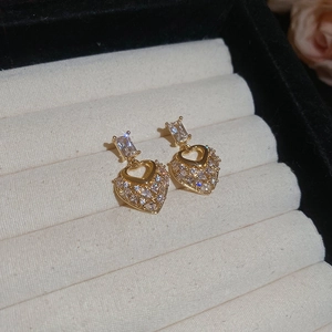 Detailed view of heart-shaped gold drop earrings with sparkling cubic zirconia on beige velvet