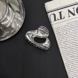 Close-up of a silver irregular metal hair claw clip on black leather with a sleek metallic finish