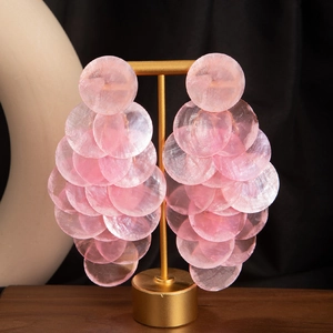 Pink cascading shell layered hoop earrings for women on a golden display stand
