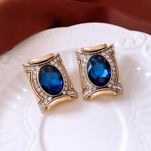 Detail of vintage gold earrings with oval blue gemstones and rhinestone accents on a ceramic tray