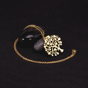 Detailed shot of a gold Tree of Life pendant necklace on dark stones with fine link chain