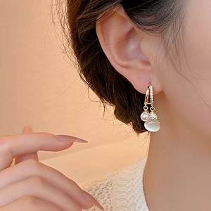 Close-up of gold gourd drop earrings with pearl and cat-eye stone on a female model