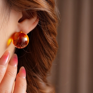 Close-up of translucent orange spherical resin earring with natural amber texture