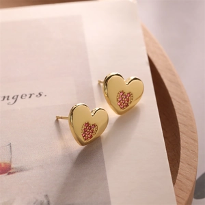 Close-up of gold heart stud earrings with micro-set red zircon on wooden tray