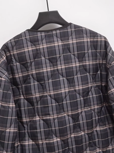 Détail macro de la veste matelassée à carreaux montrant les coutures grises et roses