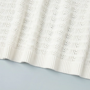 Detailed macro of white knit hem featuring geometric hollow patterns and ribbed edge finish