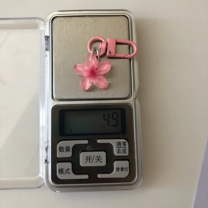 Macro shot of a pink flower keychain on a digital scale showing weight of 4.9 grams