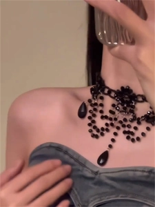 Detail of black beaded choker necklace featuring teardrop pendants and floral centerpiece