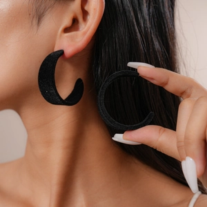 Detail of vintage black flocked C-shaped earrings worn by a model in soft lighting