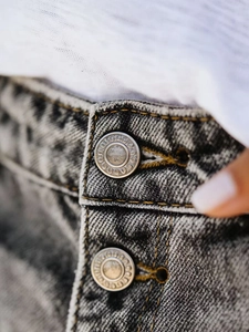 Close-up of snow wash denim shorts featuring double silver buttons and contrast stitching