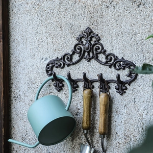 Vintage European black cast iron wall rack with four hooks on a rustic concrete wall