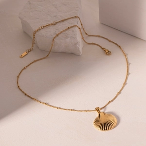 Gold stainless steel scallop shell necklace on white stone with beaded chain