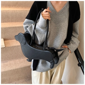 Detail shot of a black leather sausage dog shaped tote bag worn by a model in a cozy room